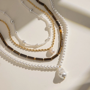 Close-up of layered stainless steel necklace with white pearls and brown tiger eye beads