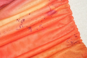 Detailed macro view of gradient mesh fabric with dark ink splatters and pleated texture