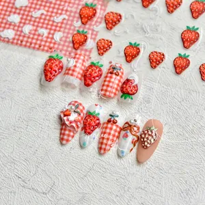 Detailed view of 3D embossed strawberry and red plaid press-on nails with pearl accents