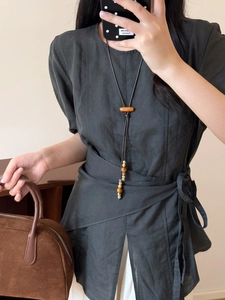 Gros plan d'un collier vintage en perles de bois et pompons sur un haut en lin doux