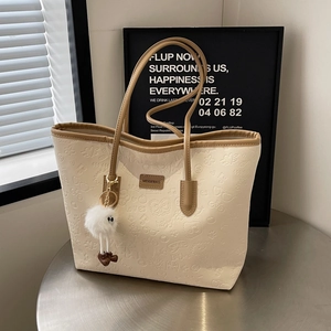 Detail of cream tote bag with embossed patterns and decorative plush charm on side