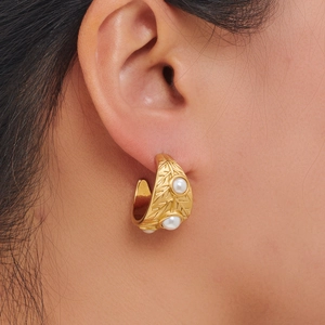 Golden C-shaped hoop earrings with leaf vein texture and three pearls on model