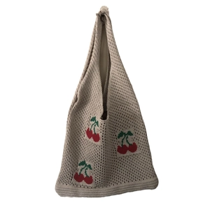 Detailed view of beige knit tote bag featuring red cherry embroidery patterns