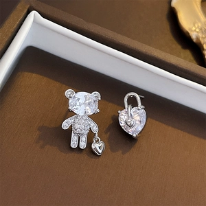 Macro shot of asymmetric silver teddy bear and heart earrings with sparkling zircons