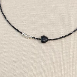 Beaded necklace with a black heart pendant and silver wire accents on a textured cloth