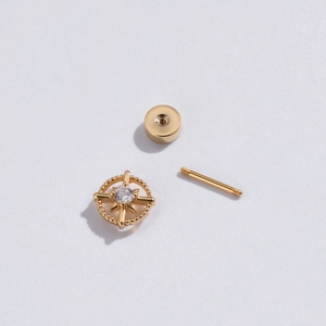 Détail d'une boucle d'oreille étoile dorée avec zircon central sur fond blanc