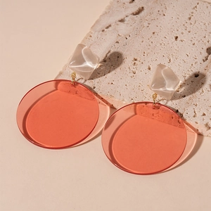 Close-up of geometric resin earrings with cream square studs and red translucent circles