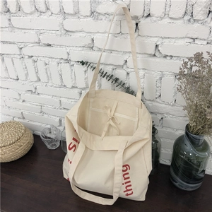 Detail of cream canvas tote bag showing interior pocket, tie closure, and red lettering