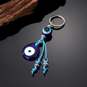 Ethnic blue evil eye keychain with glass beads and tassels on a black reflective surface