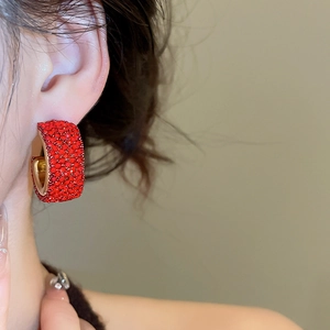 Close-up of red rhinestone encrusted C-shaped gold earrings worn on a model's ear