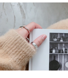 Close-up of minimalist silver geometric rings worn by model holding a book