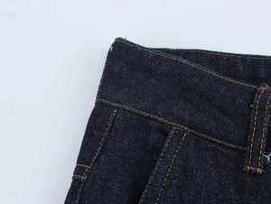 Détail de la taille en denim bleu foncé avec coutures orange et texture du tissu