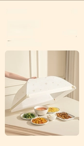 Détail d'une main soulevant la cloche alimentaire pliable blanc cassé sur une table
