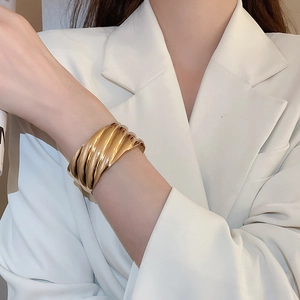 Détail de la texture ondulée sur un large bracelet doré en métal porté par un mannequin