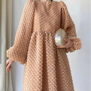 Detail of warm apricot long sleeve dress with 3D floral petal texture and loose silhouette