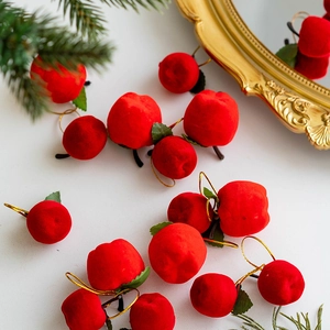 Red flocked Christmas apple ornaments with green leaves and gold strings on white background