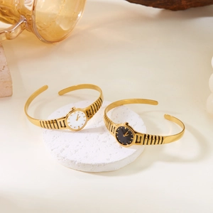 Detailed macro view of gold-plated watch style cuff bracelets on a textured stone surface