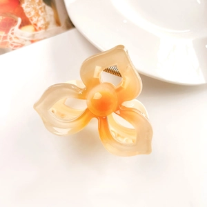 Close-up of translucent orange plumeria hair claw clip with golden metal spring