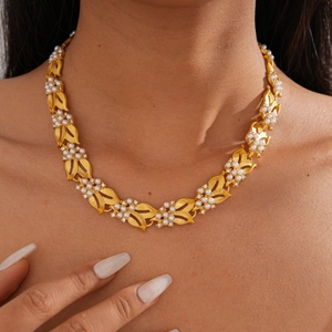 Detailed close-up of vintage golden leaf necklace with white pearls on a model neck