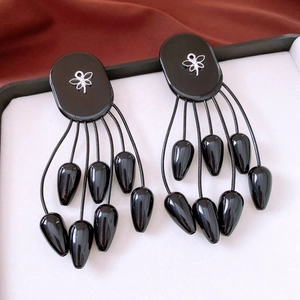 Détail de boucles d'oreilles bohèmes à pompons avec clou ovale noir et motif papillon