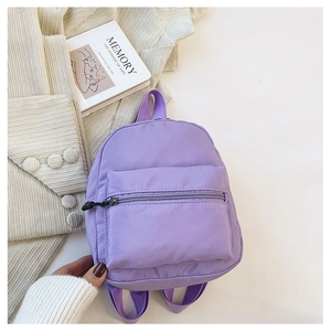 Flat lay of light purple nylon mini backpack on a table with a book and corduroy jacket