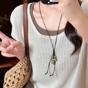 Detail of Dalmatian stone flower pendant on black wax cord necklace over beige knitwear