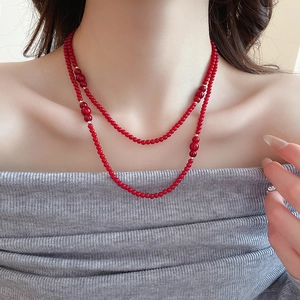 Detail of a double-layered deep red beaded necklace with golden metal spacers on a model