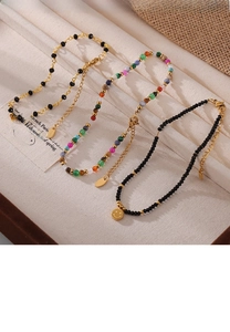 Detail of colorful beaded anklet with black beads and a golden smiley face charm