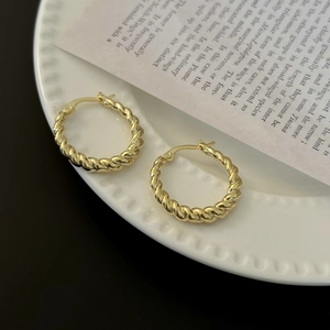 Close-up of vintage French gold twist hoop earrings on a decorative white ceramic plate
