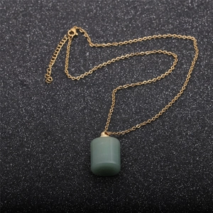 Detail of a green stone perfume bottle pendant with a gold chain on dark textured background