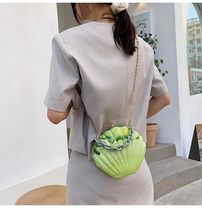 Detail of shell-shaped gradient green acrylic bag with gold chain strap on a model
