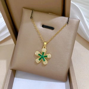 Close-up of gold flower necklace with green gemstone and pavé diamonds on white silk