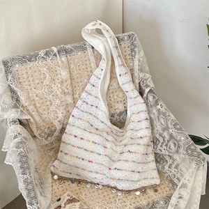 Detail of bohemian striped knit tote with shell charms on white lace background
