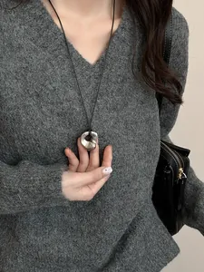 Detail of silver irregular hollow pendant on black cord over a grey sweater fabric