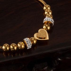 Macro detail of golden beaded bracelet with frosted heart pendant and zircon accents