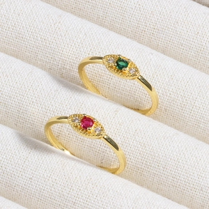 Detail of gold evil eye rings with green and red zircon stones in a beige display box