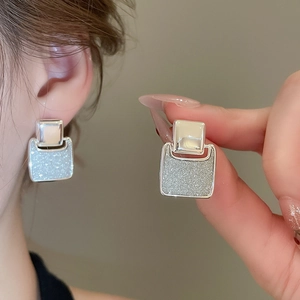 Detail view of silver square stud earrings with shimmering matte texture on ears