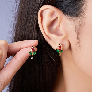 Detail of tulip stud earrings with red petals and green leaves held by fingers