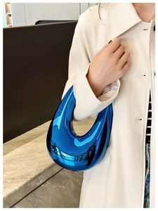 Blue glossy acrylic clutch bag with reflective mirror finish held by a model in a coat