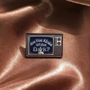 Vintage TV enamel pin with Are You Afraid of the Dark slogan on brown silk background