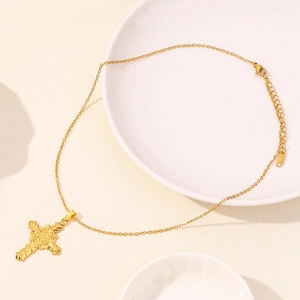 Detailed macro shot of a golden cross necklace with rose relief on a white ceramic plate