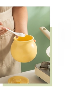 Close-up of a yellow ceramic seasoning jar with lid and spoon holding salt in a kitchen