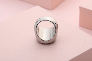 Polished silver stainless steel thick band ring displayed on pink geometric props