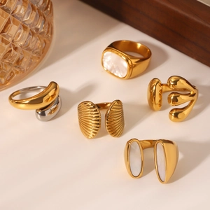 Set of five gold stainless steel rings with white shell inlay on a warm-toned background