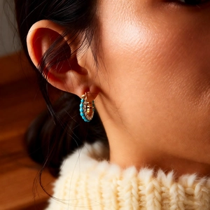 Macro view of gold plated hoop earrings with turquoise stones and sparkling zircons