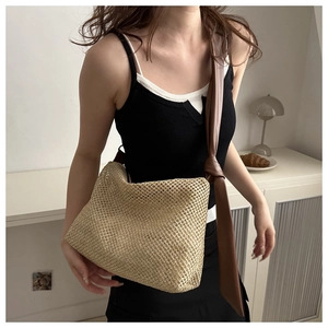 Close-up of woven straw tote bag with brown faux leather knotted shoulder strap detail