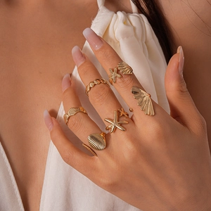 Detailed view of gold starfish and shell rings set on model hand for beach style