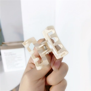 Close-up of small square hair claw clip in beige resin with metallic spring detail