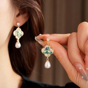 Détail de boucles d'oreilles trèfle avec paysage en émail vert et perle blanche pendante