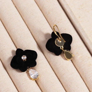 Macro shot of geometric suede flower earrings with zircon tassels on beige velvet